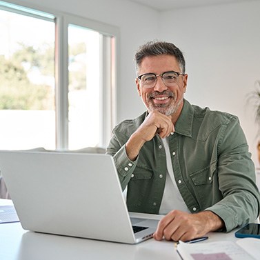Man with glasses smiling while working on laptop