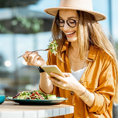 Woman smiling while looking at her phone and eating