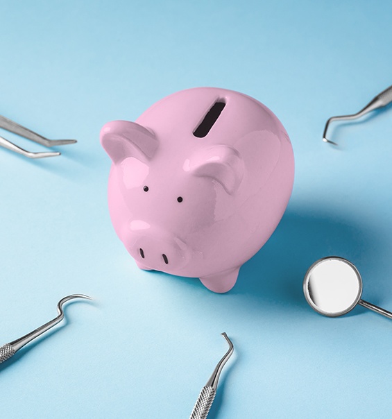 A pink piggy bank surrounded by dental tools on a blue background