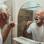 An older man is standing in front of his mirror brushing his teeth in his bathroom in West Palm Beach