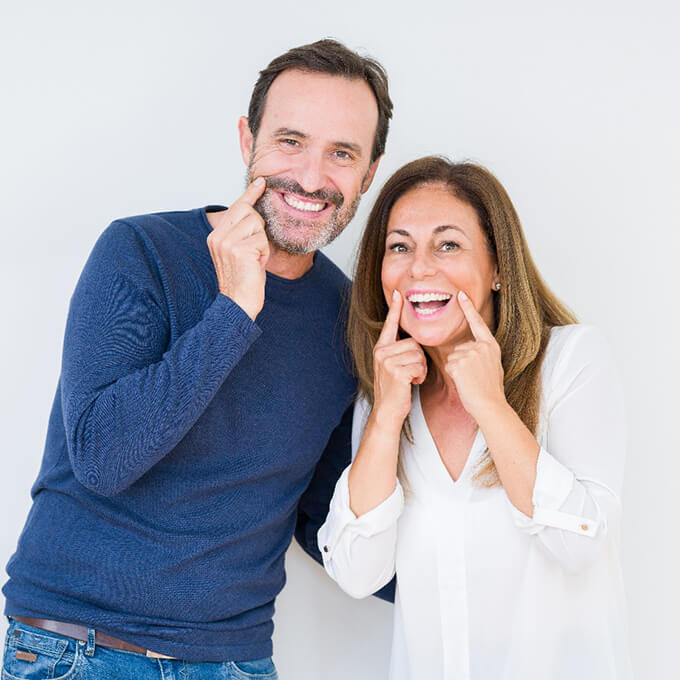 couple pointing to their smiles with dental implants in West Palm Beach