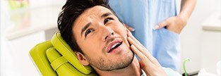 Man in dental chair holding cheek in pain before T M J therapy for jaw pain