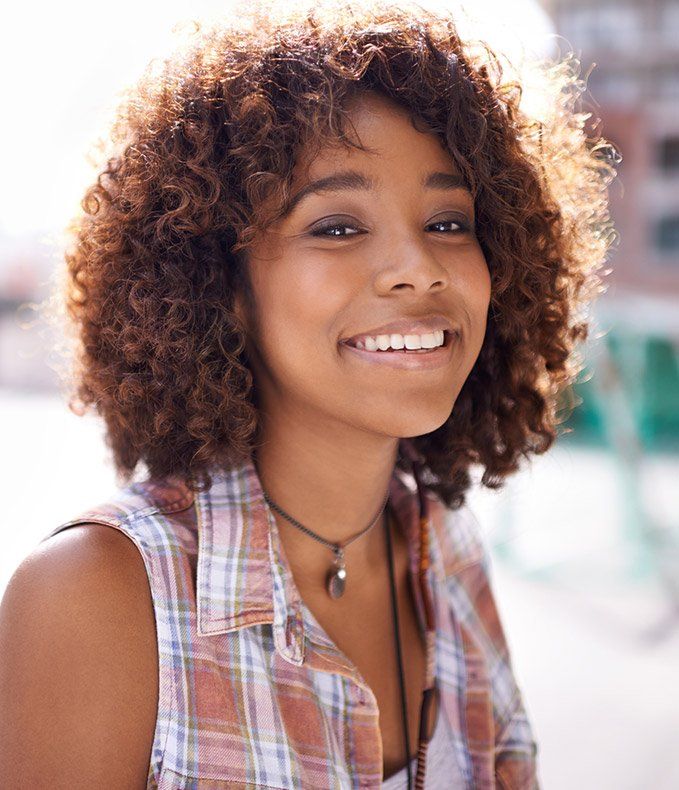 Woman with curly hair smiling outdoors on sunny day