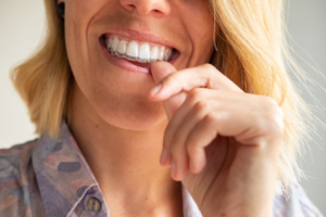 a patient smiling and inserting her Invisalign aligner