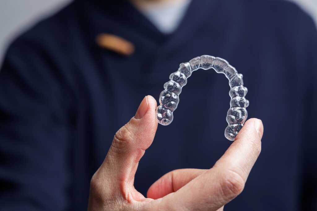 Man in navy scrubs holding clear aligner. 