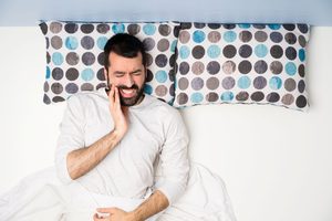 Man in bed squinting in pain touching jaw
